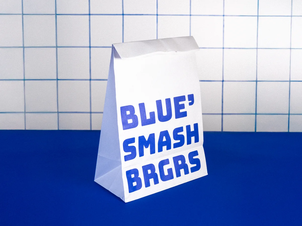 Bolsa de papel de Blue Smash Brgrs sobre el suelo azul del local