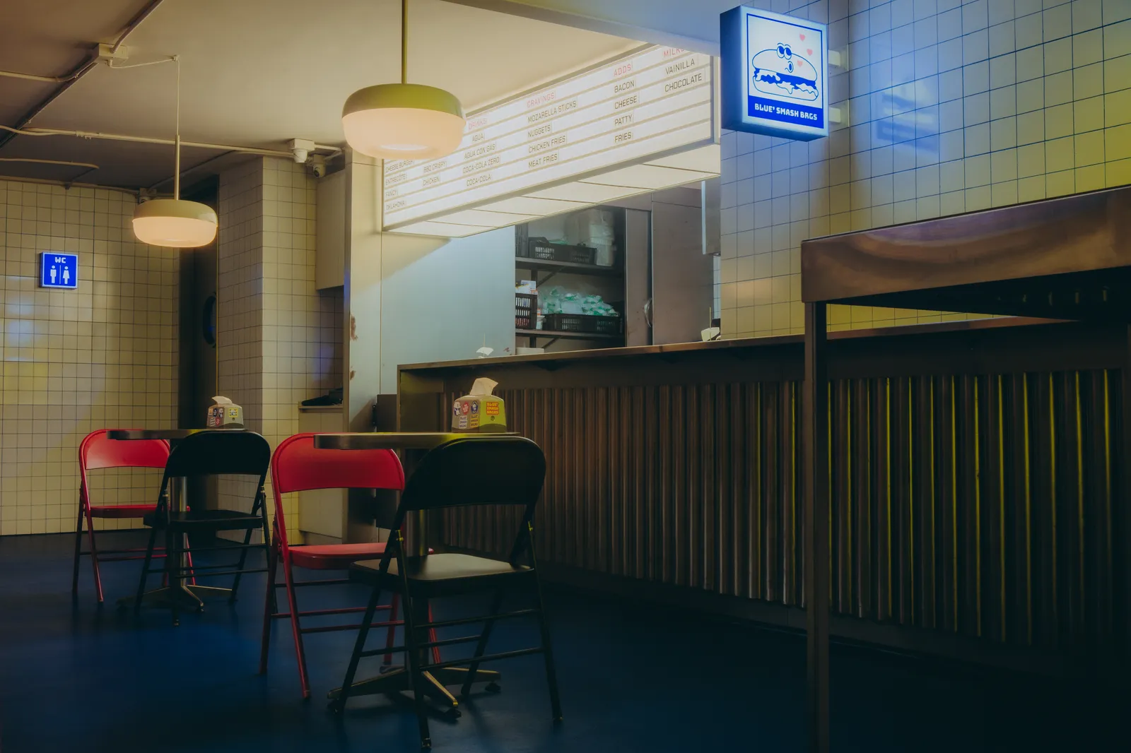 Interior del local de Blue Smash Burger en Manila: mesas, sillas y el aviso luminoso sobre la barra